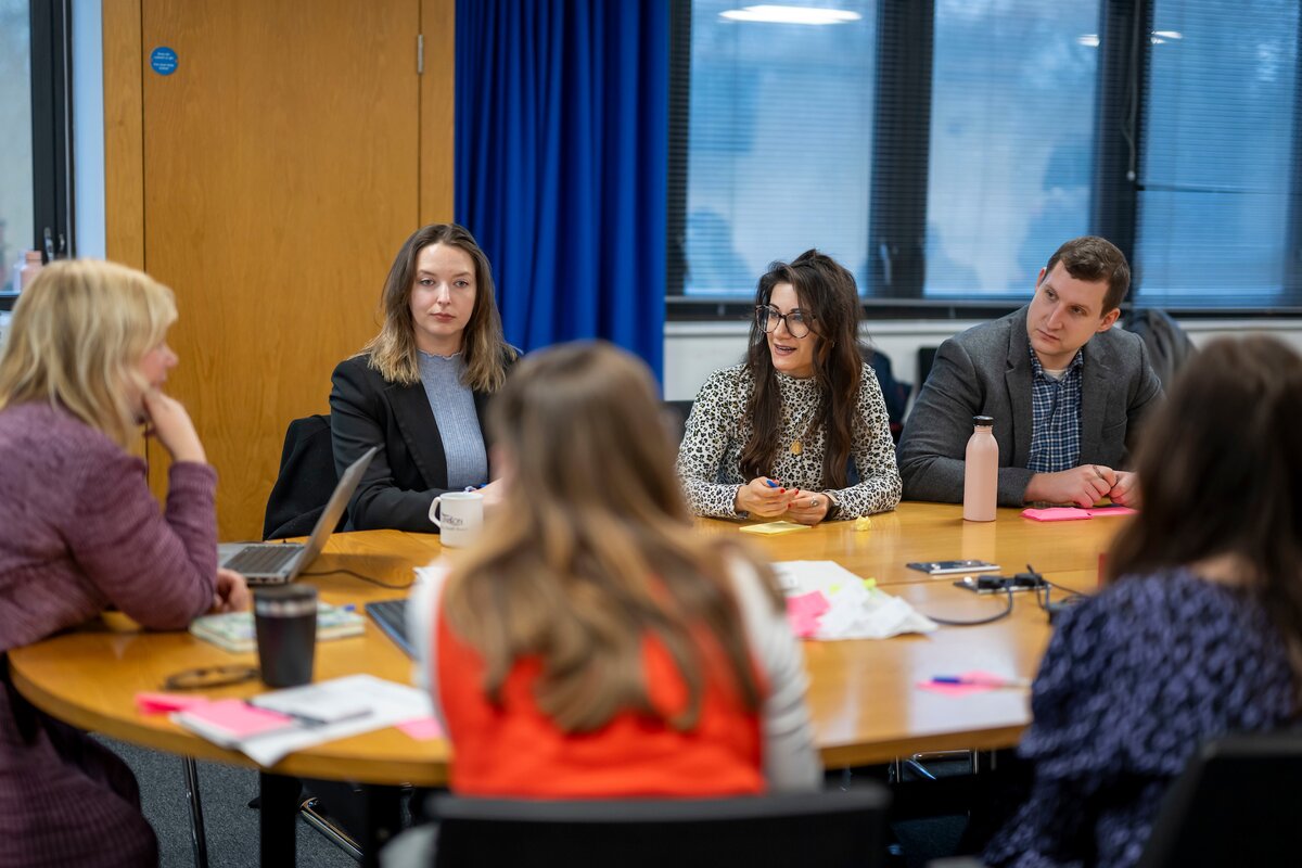Shayda Kashef sitting at a round table with five other people at a meeting to discuss public engagement. 