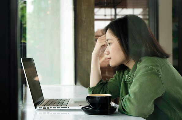 A woman looking at her laptop with a mug of coffee beside her