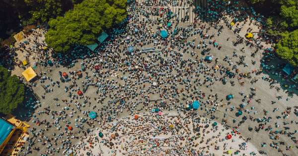 Image shows a birdseye view of a road and roundabout full of people, surrounded by trees