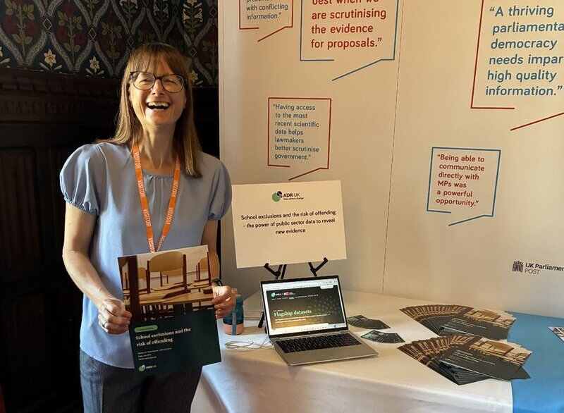 Vickie Barrett standing in front of the ADR UK stand at Evidence Week, holding a copy of her policy briefing