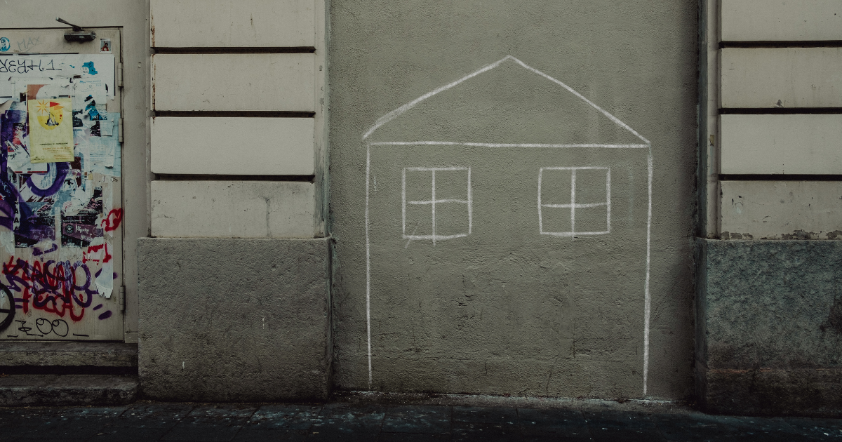 A chalk drawing of a simple house on a grey wall
