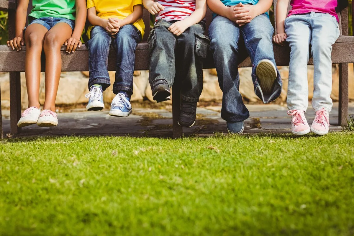 A row of children sitting on a bench on a lawn
